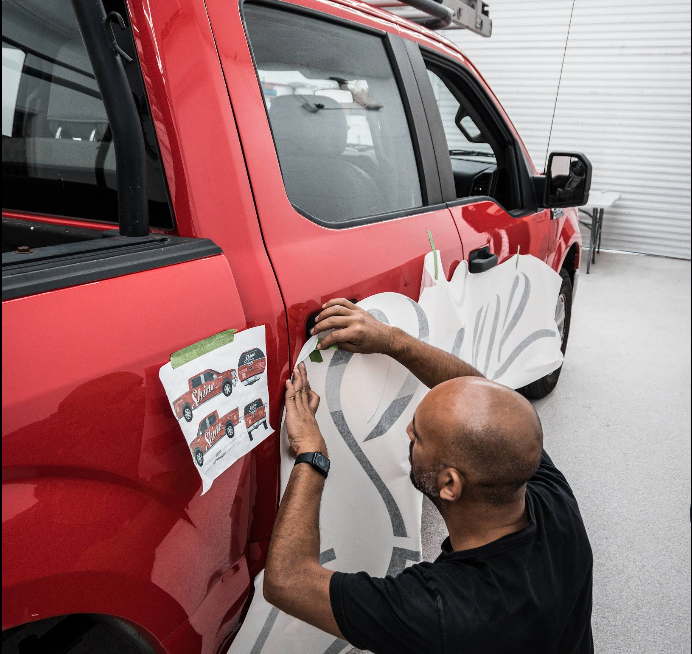 VinylSquad installer applying vinyl graphics by hand on a red pickup truck